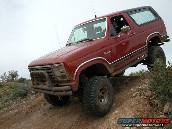 Red Ford Bronco climbing a dirt hill with large tires and a brush guard