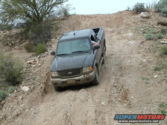 Dark gray Ford Ranger driving up a dirt hill, front 3/4 view
