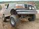 1993 Ford Bronco - A lifted 1992 Ford Bronco navigates a dusty, off-road trail with a person visible in the background.