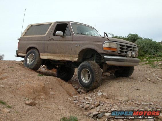 Brown 1993 Ford Bronco climbing a dirt hill with large tires