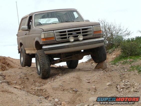 Brown Ford Bronco off-roading, front passenger tire on a rock