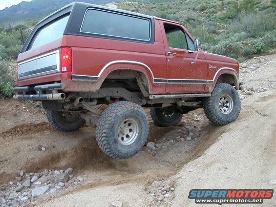 Red Ford Bronco with lifted suspension and off-road tires driving on a dirt trail
