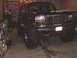 1996 Ford Bronco - Green Ford Bronco with oversized tires is lifted by a jack in a garage.