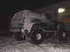 1996 Ford Bronco - A snow-covered Ford Bronco sits parked outside a building during the night.