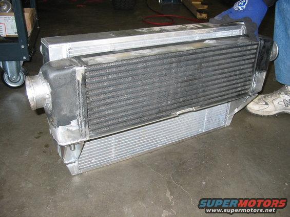 Aluminum intercooler with black end tanks and ribbed core, held by a gloved hand