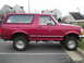 1994 Ford Bronco - A red Ford Bronco with a lifted suspension and off-road tires is parked on a curb.