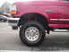 1994 Ford Bronco - Close-up of a red 1994 Ford Bronco's front fender and tire, showing aftermarket shocks.