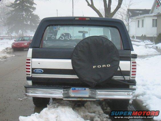 Rear view of a 1992 Ford Bronco with a spare tire cover and a red car in the background