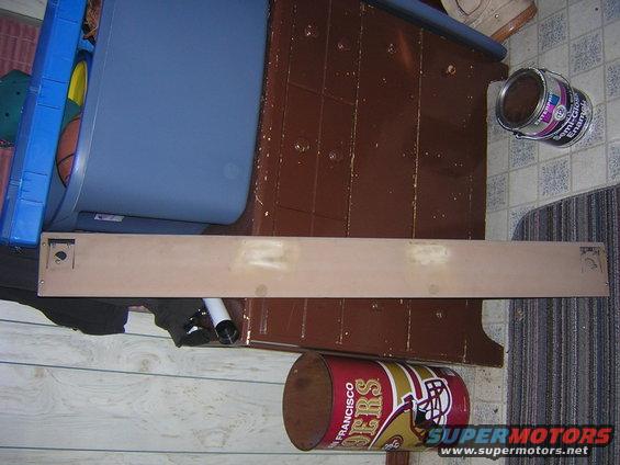 Tan panel with screw holes and a square cutout, resting on a floor