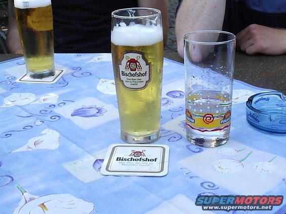 Table with two glasses of beer, an empty glass, and an ashtray on a blue patterned tablecloth