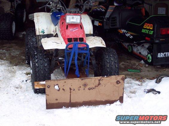 Red and white ATV with a wooden plow attachment in the snow, next to a black Arctic Cat snowmobile