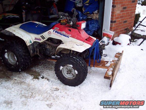 Red and white Honda ATV with a wooden snowplow attachment in the snow