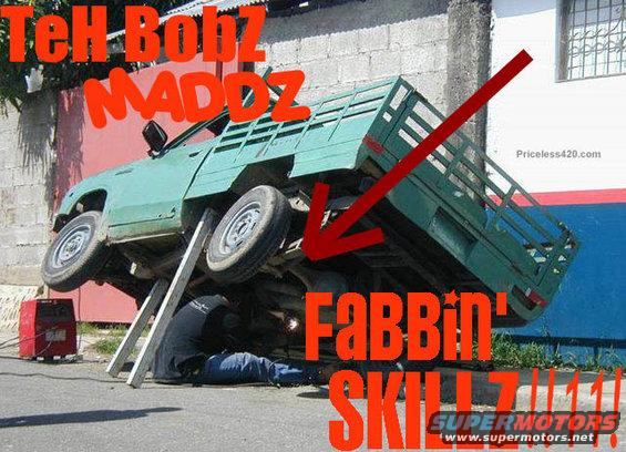 Green pickup truck tilted on its side, supported by metal ramps, with a person underneath welding