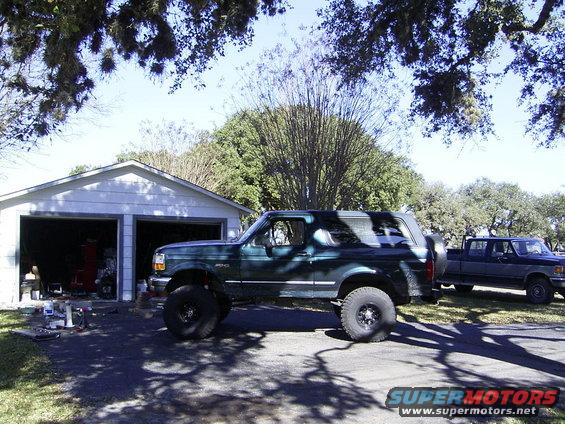 Green 1995 Ford Bronco with lifted suspension parked in driveway next to a blue pickup truck