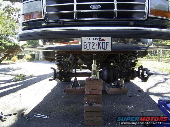 Ford truck front end lifted on jacks, suspension and axles visible. License plate reads B72-KDF