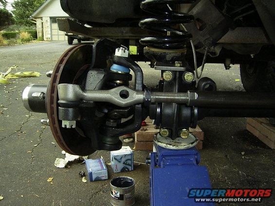 Close-up of a vehicle's front suspension and steering linkage, with a blue jack supporting the frame