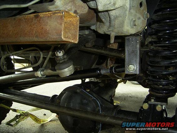 Close-up of vehicle's front axle, steering linkage, and coil spring