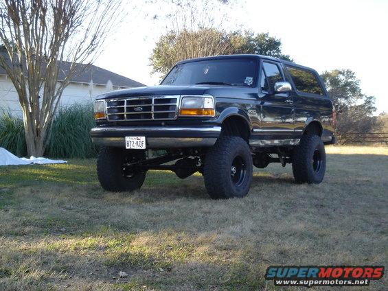 Black lifted Ford Bronco with aftermarket wheels and tires, parked on grass