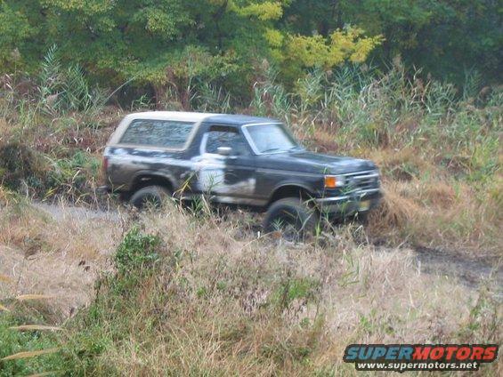 Dark Ford Bronco with white top stuck in mud, 3q front view
