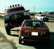 1982 Ford Bronco - A heavily modified red truck is parked next to a red hatchback, with a white SUV in the background.