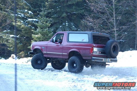 Maroon Ford Bronco with black top and spare tire on rear, driving in snow