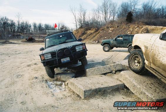 Dark SUV navigating concrete obstacles, red flag on roof