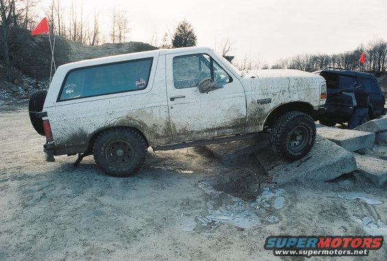 White 1995 Ford Bronco driving over rocks, another dark SUV behind it