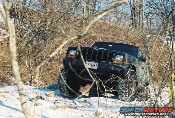Jeep Cherokee XJ with lifted suspension and off-road tires driving through snow and rocks