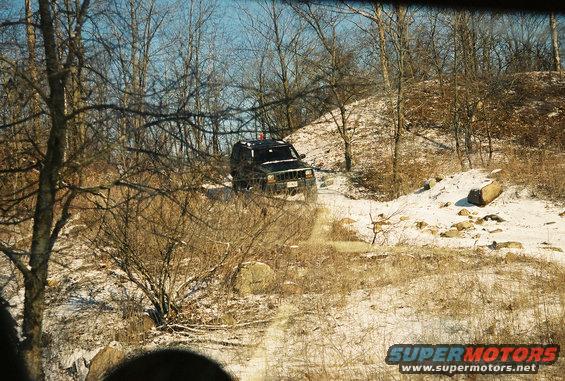 Black SUV driving on a snowy trail, trees and rocks visible