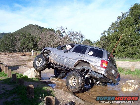 Silver Jeep Grand Cherokee with lifted suspension and large tires navigating an off-road obstacle course