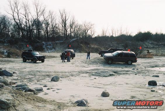 Several SUVs and trucks parked in a dirt lot with trees in the background