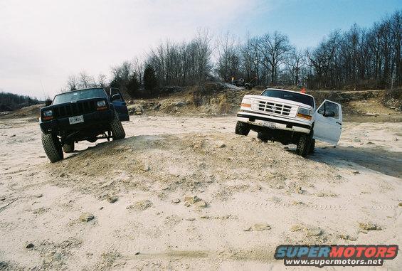 Black Jeep Cherokee and white Ford F-150 climbing a dirt hill off-road
