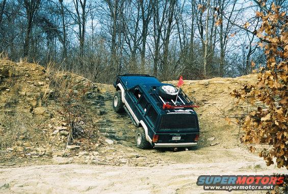 Dark blue SUV with spare tire on roof rack climbing a dirt hill