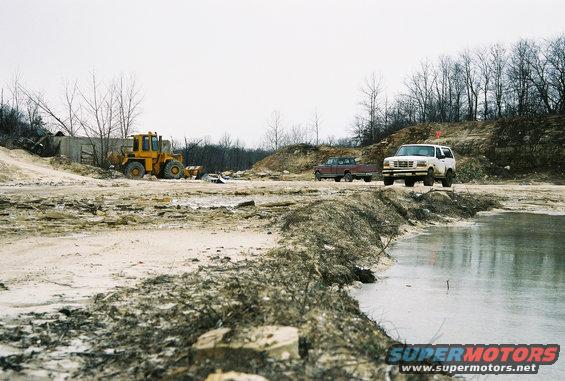 White SUV and red pickup truck at a construction site with a yellow loader