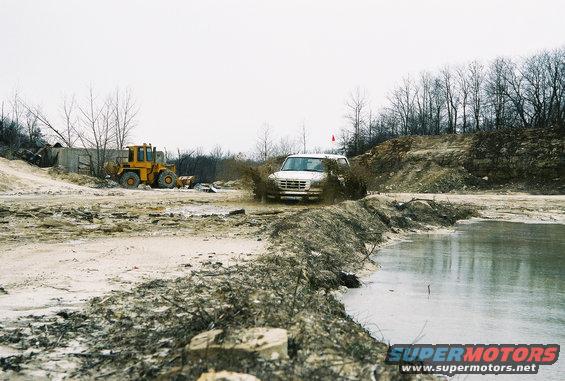 White SUV splashing mud, front view. Yellow loader in background