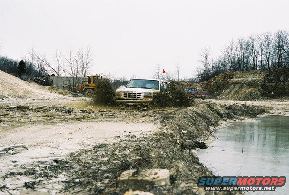 1995 Ford Bronco driving through a muddy area with a yellow loader in the background