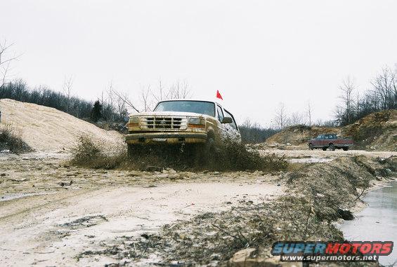 Tan Ford Bronco driving through mud, red flag on roof