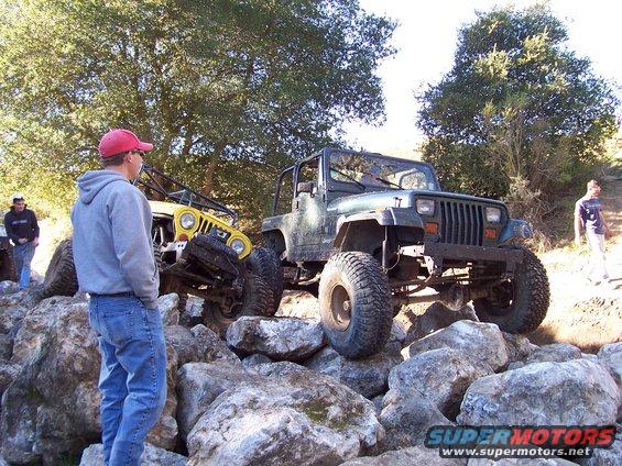 Green Jeep Wrangler and yellow Jeep CJ on rocks, with people watching