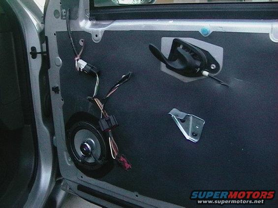 Car door panel with speaker removed, showing wiring and door handle mechanism