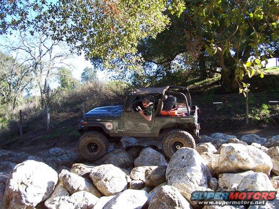 Olive green Jeep CJ-7 with a soft top navigating a rocky trail