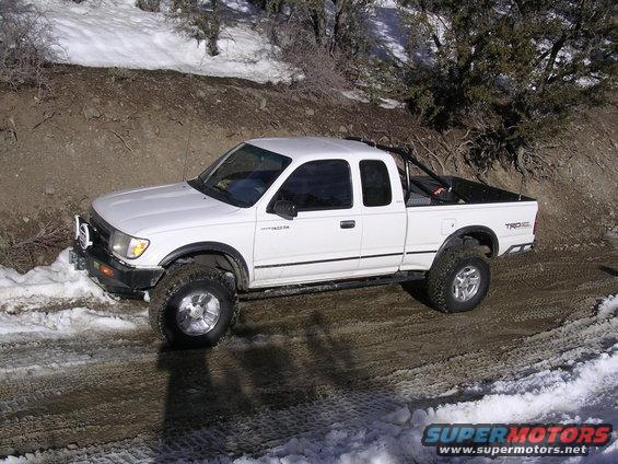 White 1999 Toyota Tacoma pickup truck with off-road tires on a dirt and snow-covered road