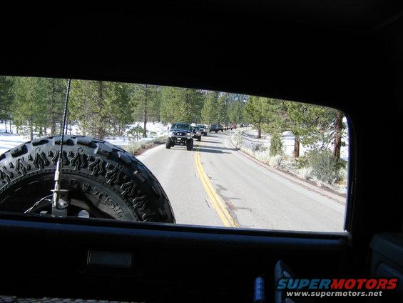 View from inside a vehicle looking out at a line of SUVs driving on a road with snow on the sides