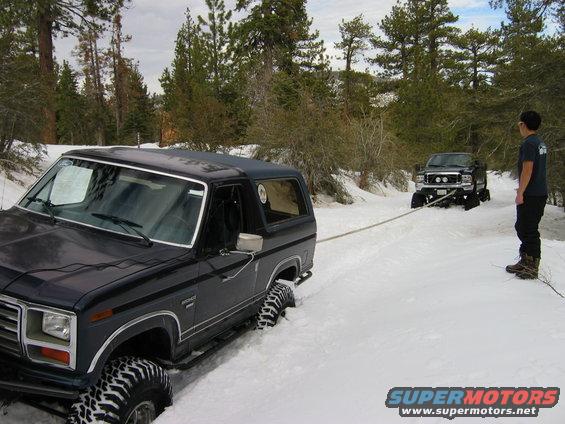 Black Ford Bronco in snow, being towed by a black Ford F-Series truck