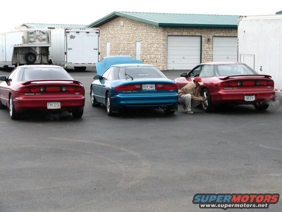Three 1994 Ford Probes parked outside a building, one with hood up, one with a person working on a wheel