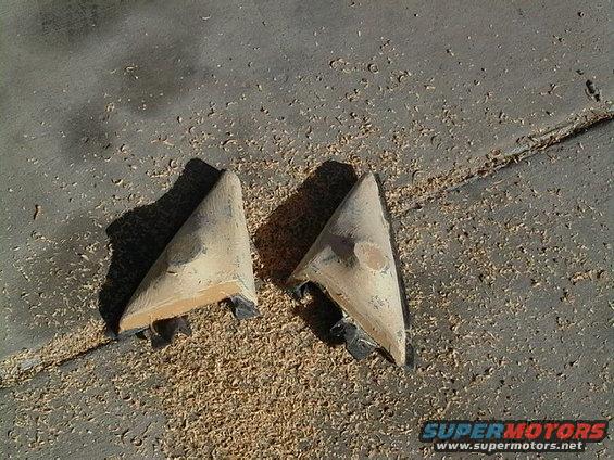two triangular car mirror housings on the ground with wood shavings