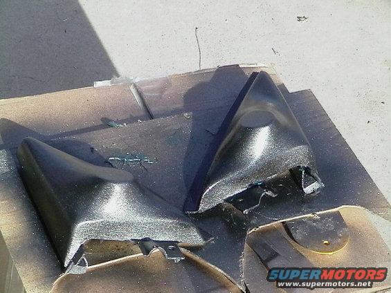 Two black car mirror housings on a surface, one with visible damage