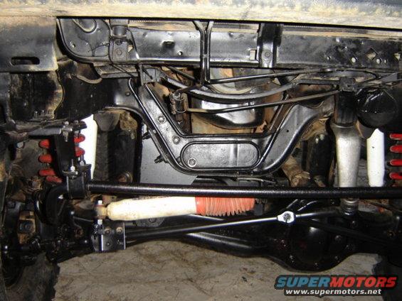 Undercarriage of a vehicle with red coil springs, black suspension components, and a white steering stabilizer with an orange boot