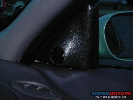Car door panel with a small speaker grille and a side mirror visible