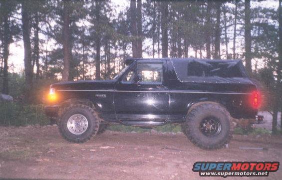 Black Ford Bronco with a soft top, lifted suspension, and off-road tires parked on a dirt road