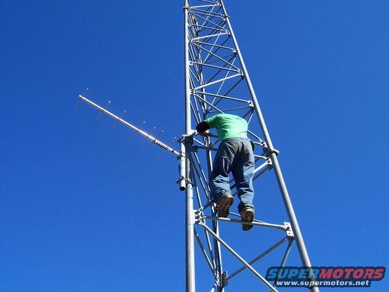 guy climbing a tall metal tower with antennas against a blue sky
